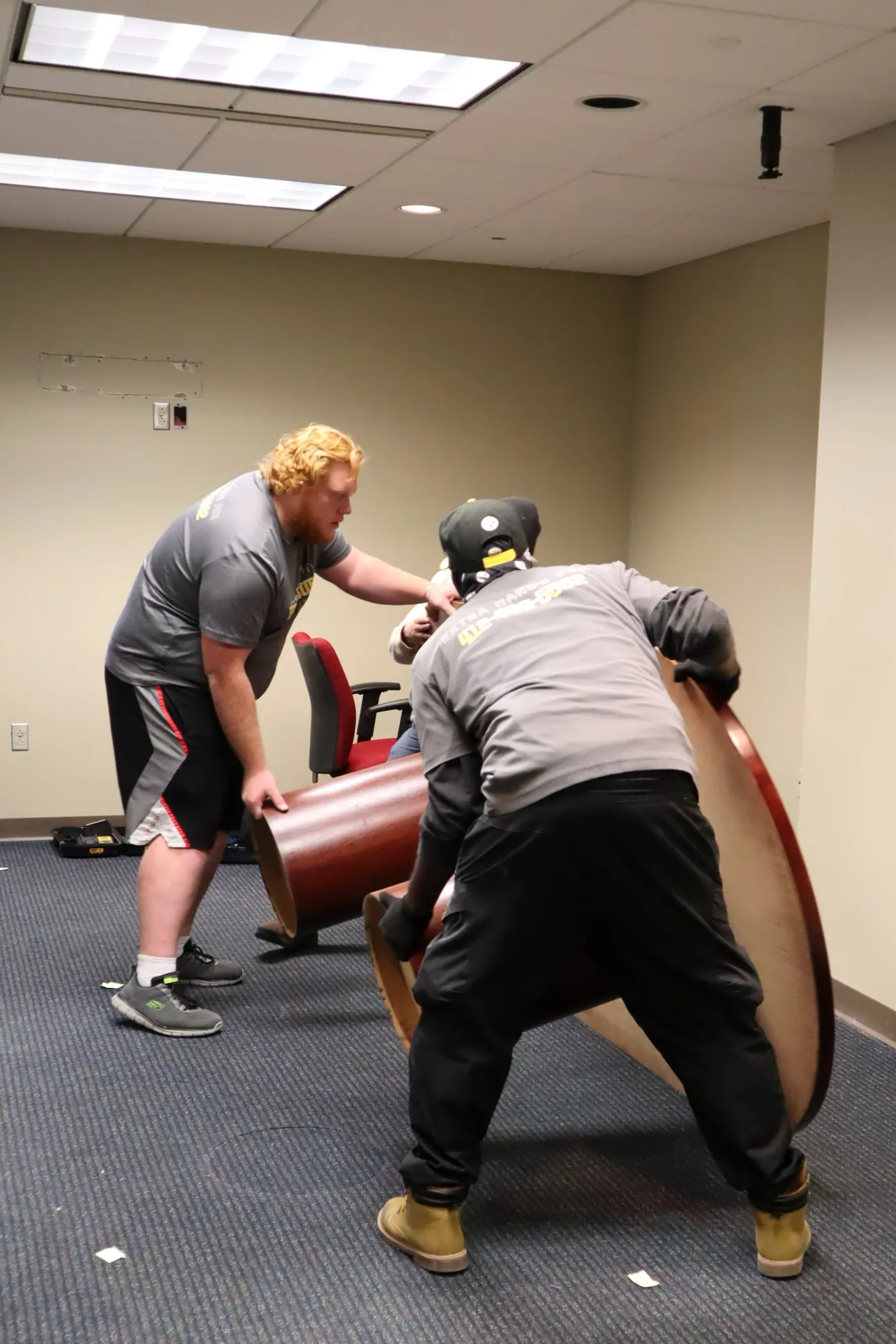 Movers carrying curved wooden office furniture through an empty office.