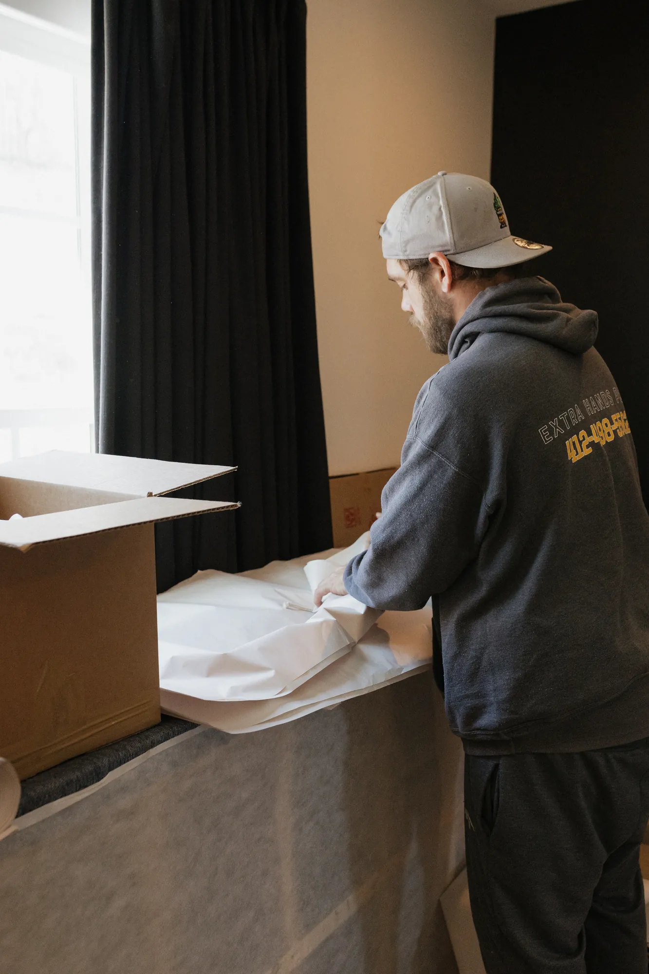 Packer wrapping household items in packing paper beside an open moving box.