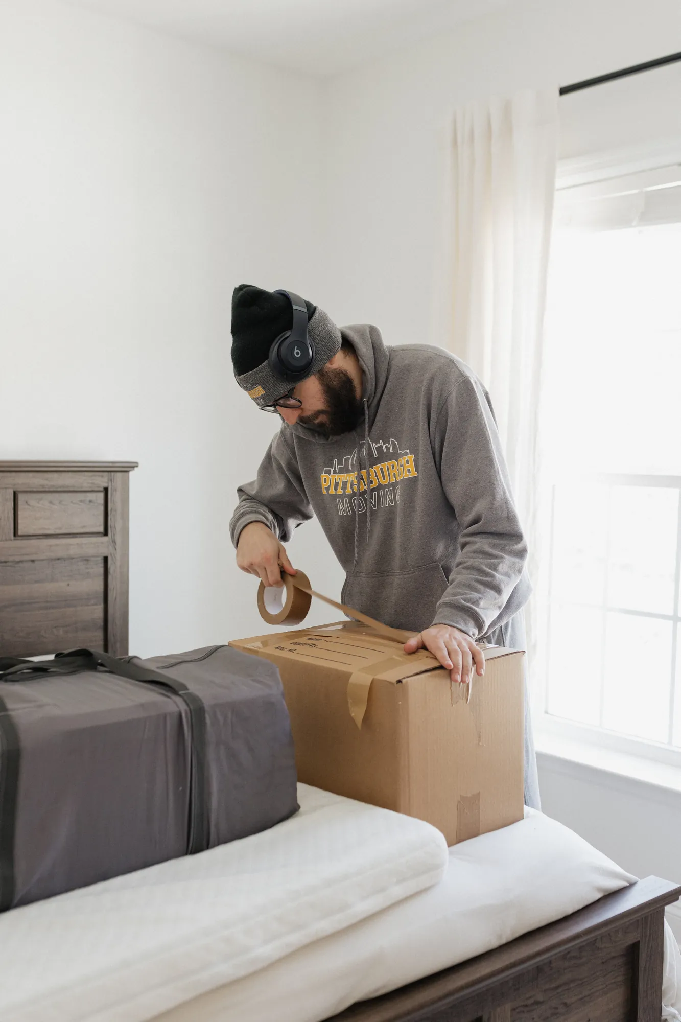 Pittsburgh Moving PGH packer taping a moving box on a bed during an in-home packing job.
