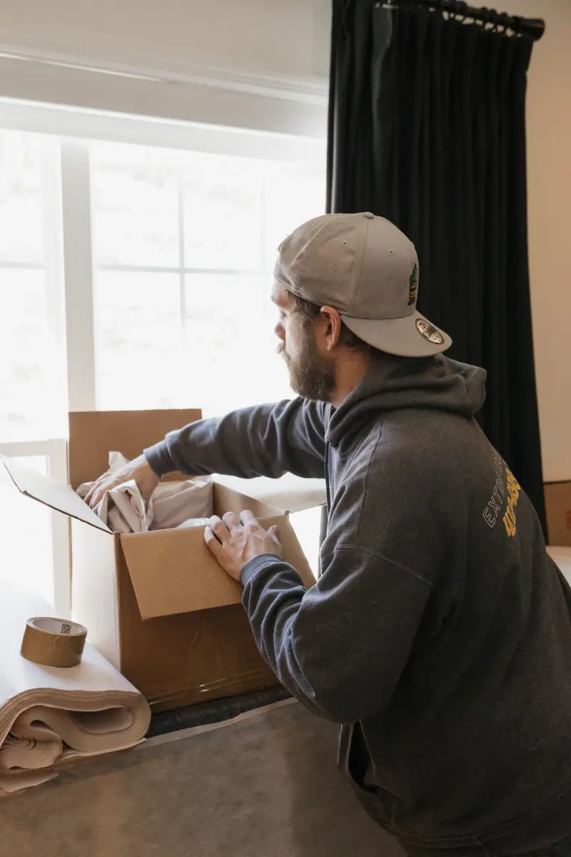 Packer placing packing paper into a moving box next to tape and folded paper.